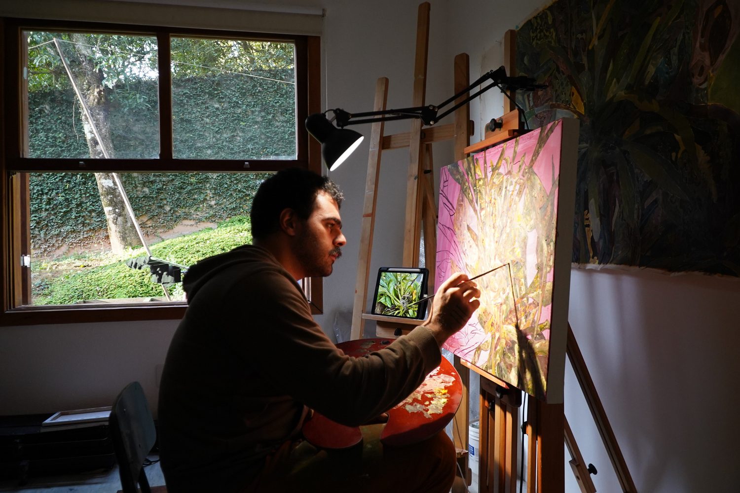 João Possos pintando no ateliê, diante da janela.