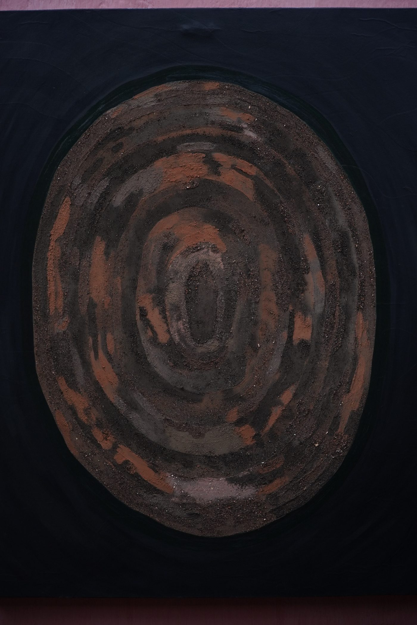 Pintura de João Possos: forma oval de pigmento de terra em camadas concêntricas sobre fundo escuro.